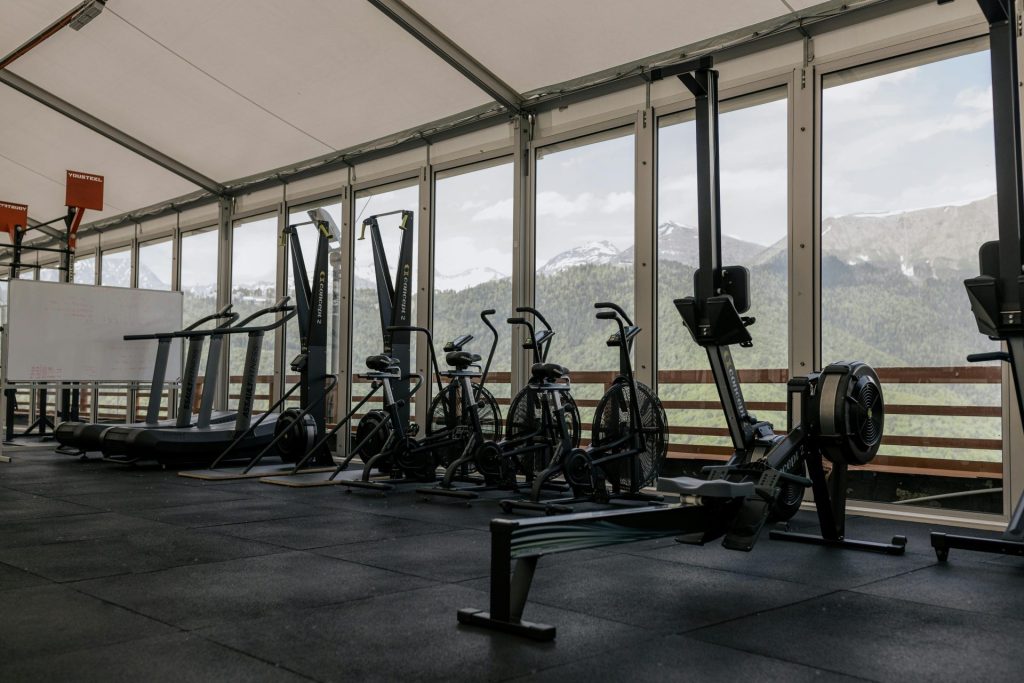 Salle de sport intérieure spacieuse dotée d'équipements de pointe avec vue panoramique sur les montagnes à l'extérieur de grandes fenêtres.